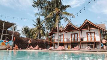 Relax by the pool surrounded by a wooden deck and lounge chairs, with a thatched-roof structure nearby.