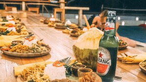 Ein Holztisch, gedeckt mit verschiedenen Speisen, einer Bierflasche und einer Kokosnuss.
