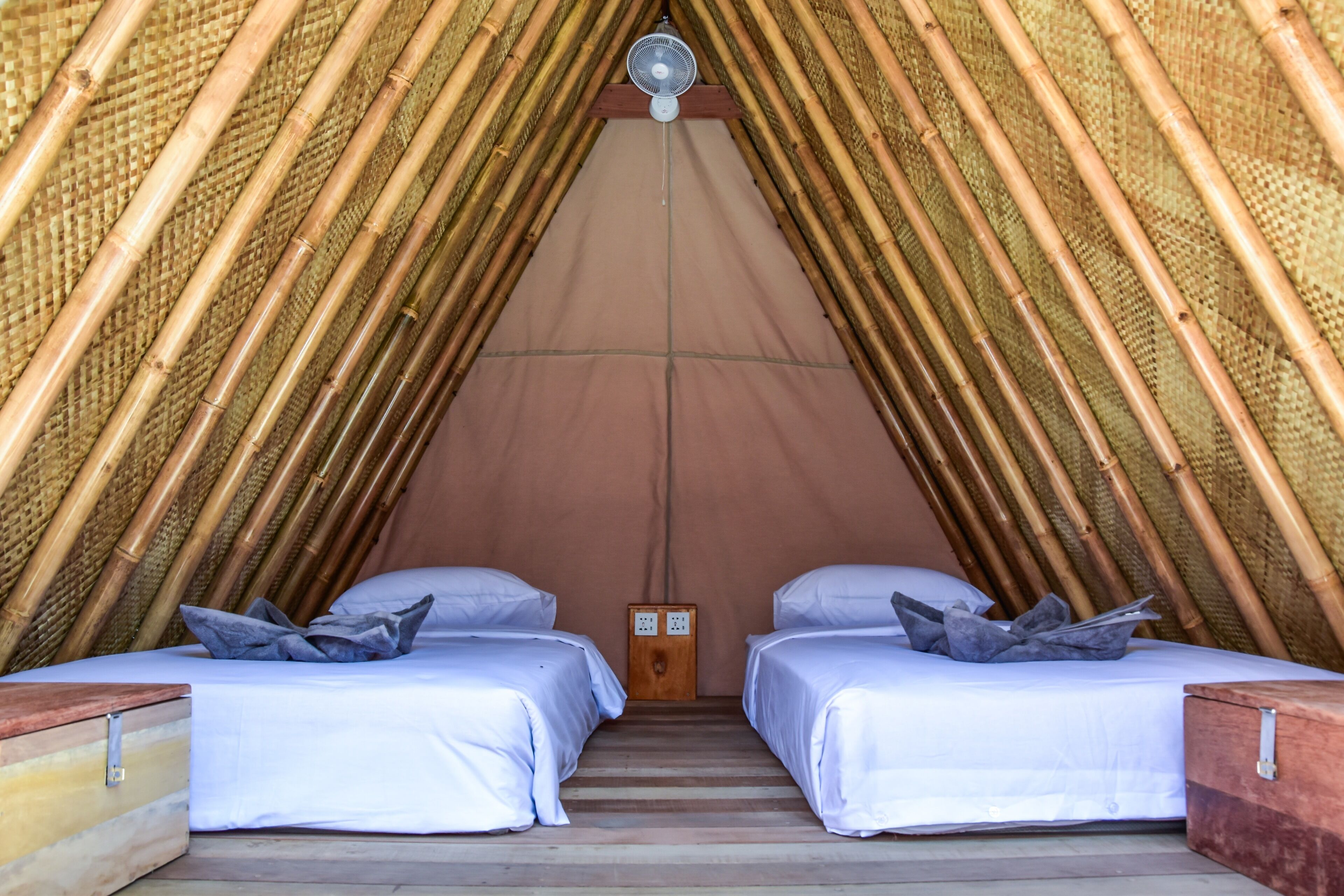 A room with two beds, a ceiling fan, and a wooden nightstand.