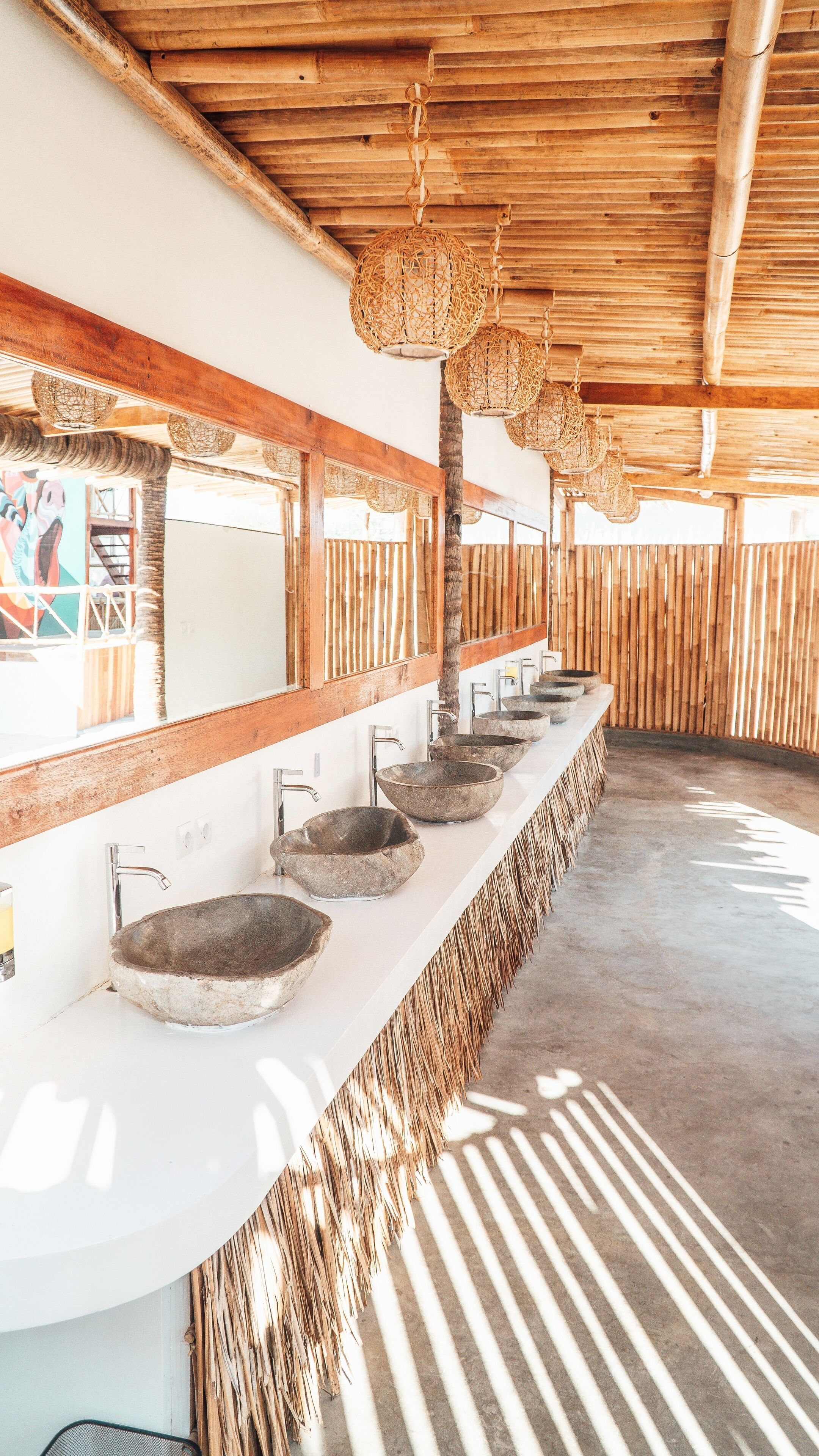 A long, white counter with multiple stone sinks and a woven fringe at the end.