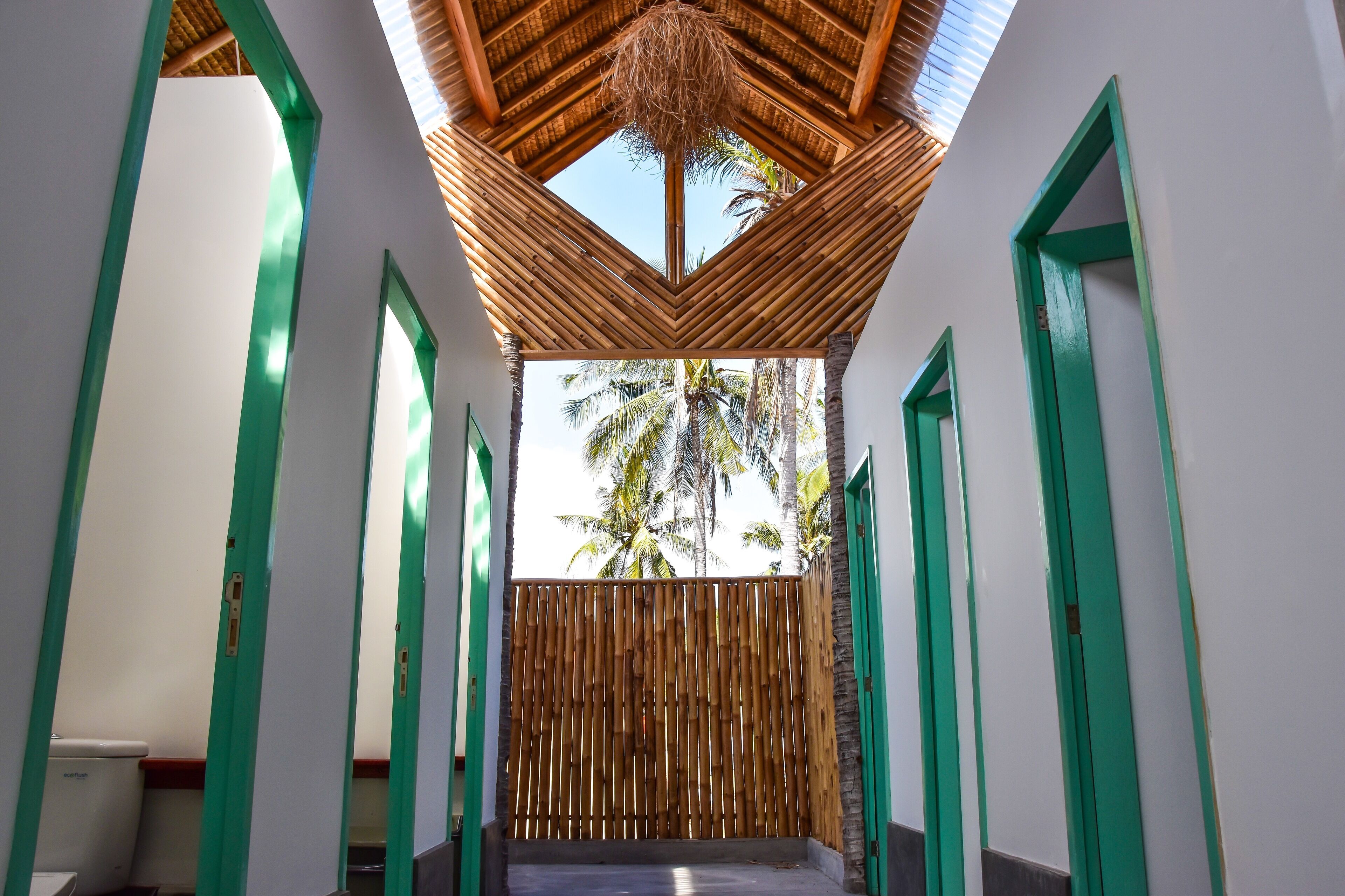 Pasillo con puertas verdes y valla de bambú que lleva a un balcón con vista a palmeras.