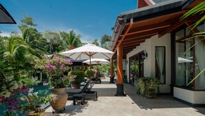 A covered outdoor area with lounge chairs and umbrellas, surrounded by lush greenery and potted plants. - Classy 4-BR Seaview Villa at Surin Beach (Choeng Thale)