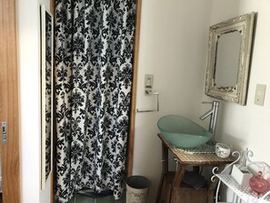 Un baño con un lavabo de vidrio, un espejo y una cortina de ducha estampada.