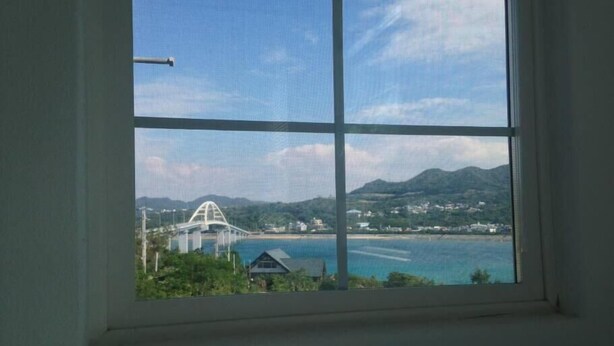 A window with a view of a bridge, water, and a hilly landscape. - Sesoko Terrace 2 (Motobu)