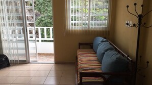 A room with a wooden bed, a fan, and a view of greenery outside.