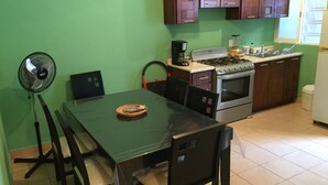 A compact kitchen with a dining table, chairs, a fan, a stove, and cabinets.