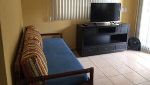 A room with a sofa, a TV on a black entertainment unit, and a fan.