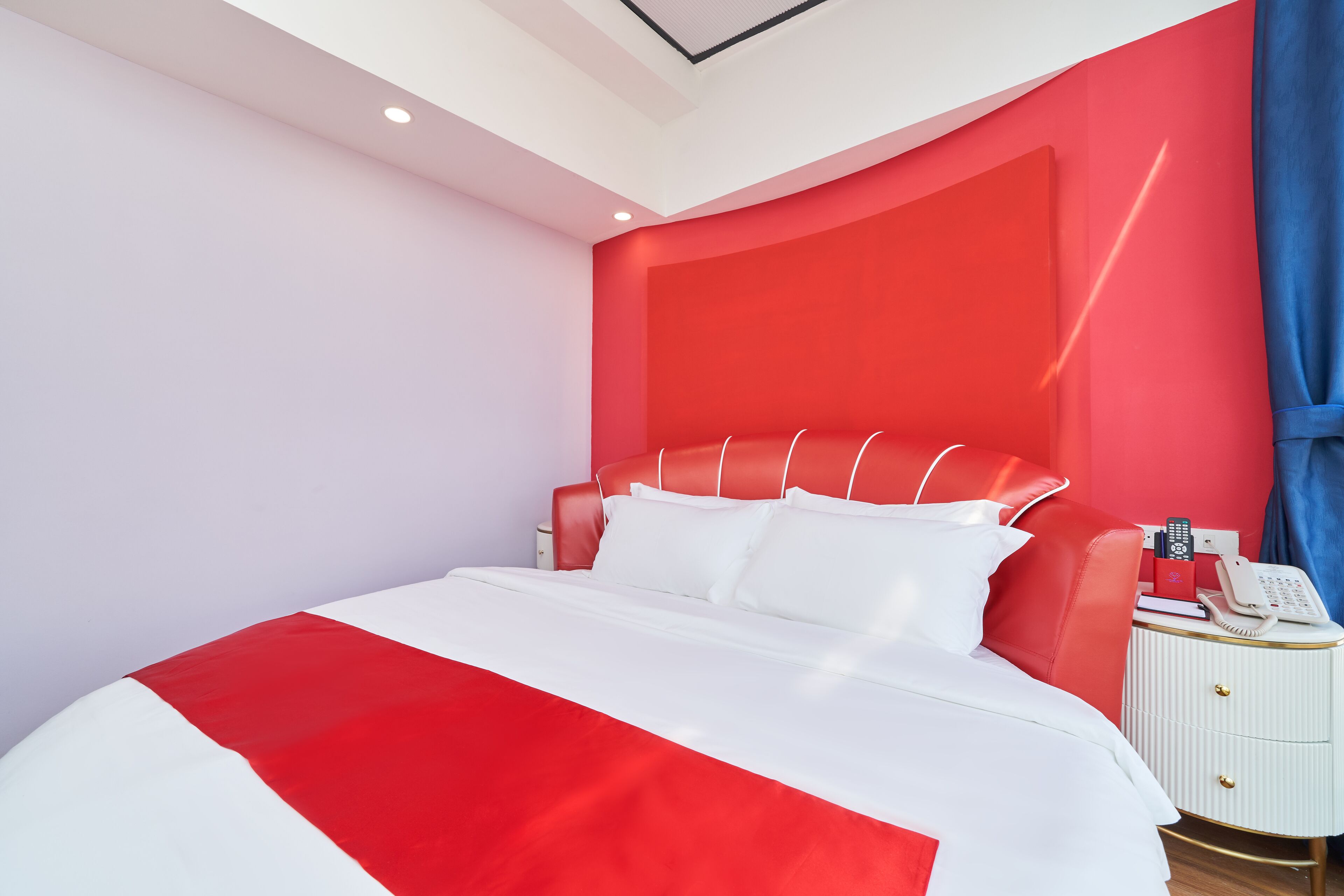A modern bedroom with a red and white color scheme, a large bed, a bedside table with a phone, and a nightstand.