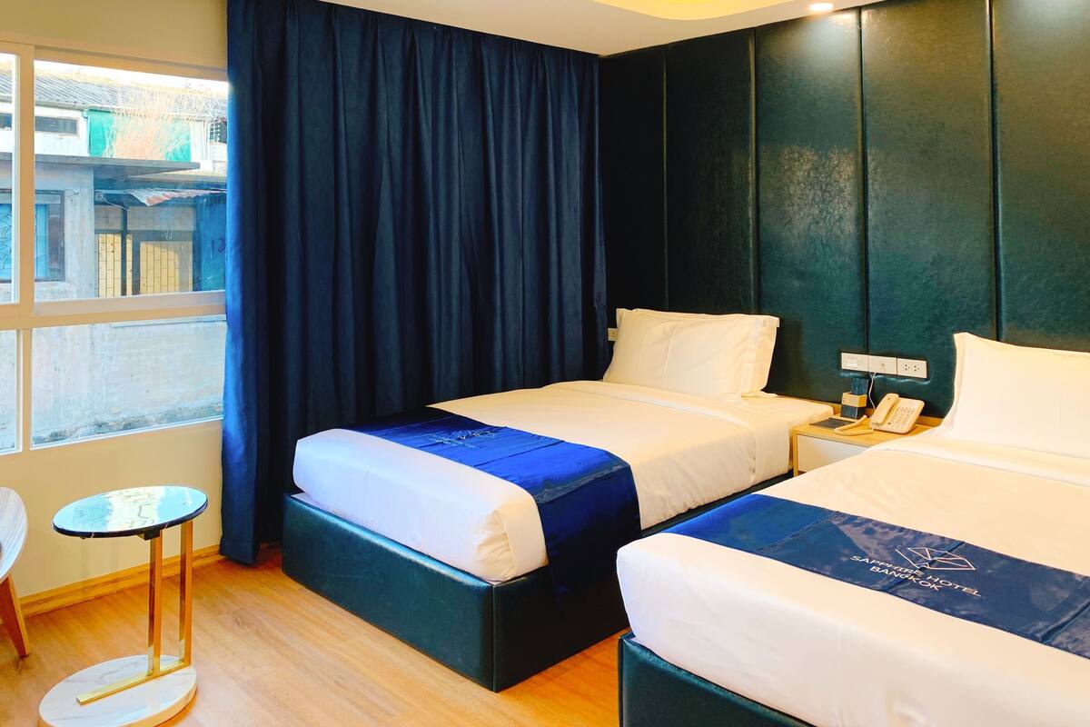 Une chambre d’hôtel avec deux lits, une petite table, une chaise et une vue sur l’extérieur.