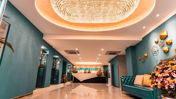 A hotel reception area with a chandelier, reception desk, and a teal sofa with a floral arrangement. - Sapphire Hotel Silom Bangkok (Bangkok)