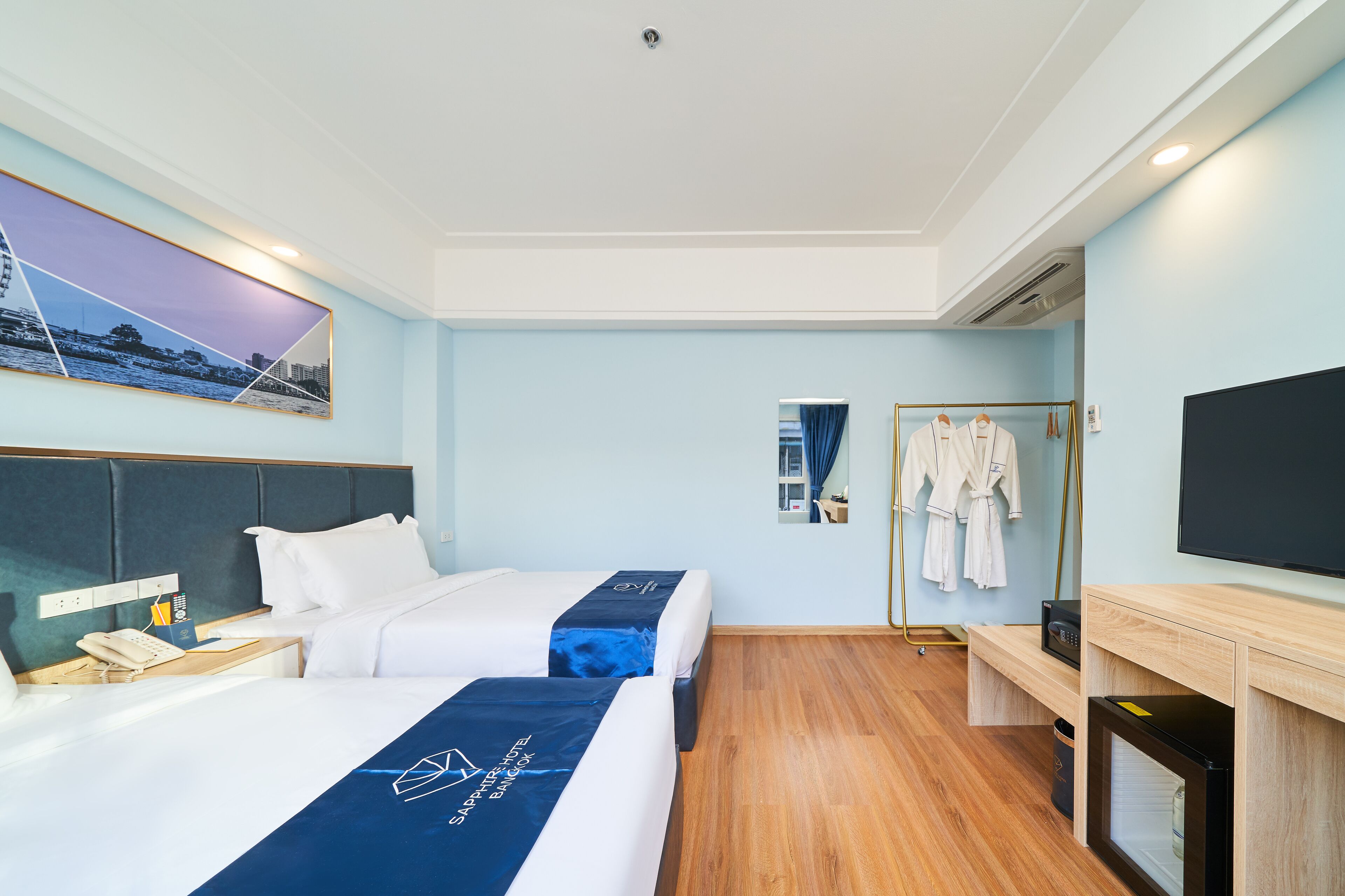 A hotel room with two beds, a TV, a desk, and a mirror.