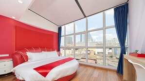 A modern hotel room with a large bed, a desk, and a view of the cityscape through large windows. - Sapphire Hotel Silom Bangkok (Bangkok)