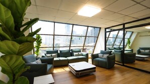 A modern office space with a large window, green sofas, and a wooden floor. - Sapphire Hotel Silom Bangkok (Bangkok)