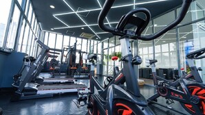 A gym with various exercise equipment, including stationary bikes and treadmills, arranged in a spacious indoor area with large windows. - Sapphire Hotel Silom Bangkok (Bangkok)