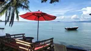 A wooden deck with a red umbrella, overlooking calm waters with a boat and palm trees. - BeauBo Beach (Ko Pha-ngan)