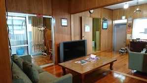 Una habitación con piso de madera, un televisor sobre un mueble de madera, un sofá y una mesa de centro con revistas.