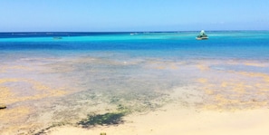 A beach with clear turquoise water, a sandy shore, and a boat in the distance. - Kokusaburo House (Onna)