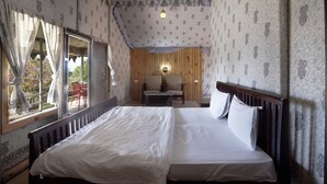Quarto com uma cama grande, cabeceira de madeira, mesa de cabeceira, uma cadeira e uma janela com cortinas.