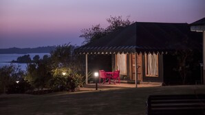 Uma área de estar coberta ao ar livre, com mesa, cadeiras, um candeeiro e vista para a água.