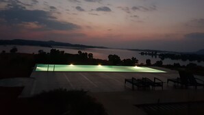 Piscina com vista para um lago e colinas ao longe ao entardecer.