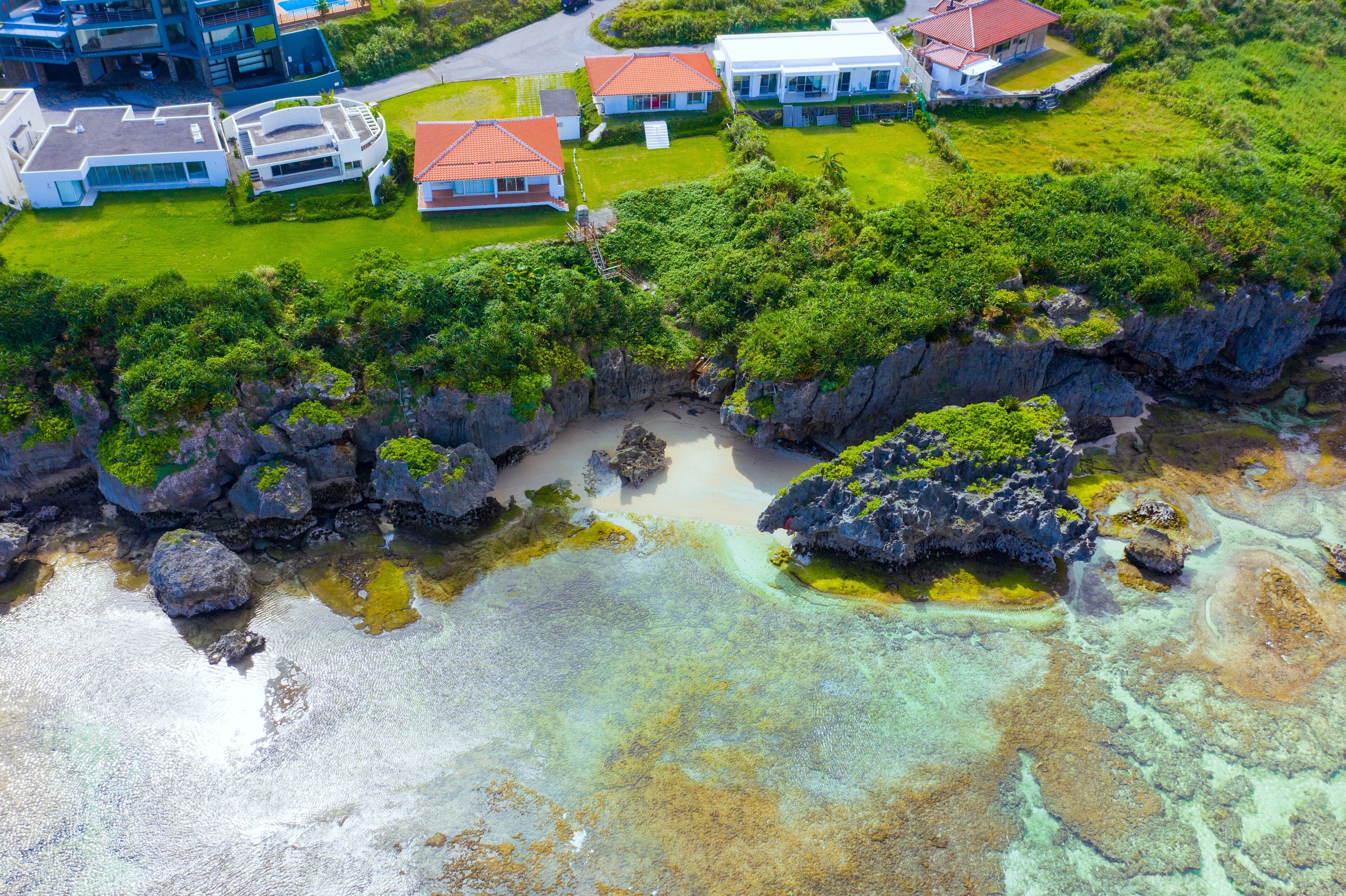 An aerial view of a coastal property with multiple houses, a rocky shoreline, and clear waters.