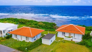 A coastal property with two white buildings featuring red-tiled roofs, a grassy lawn, and a view of the ocean. - wisteria ocean Nakijin (Nakijin)