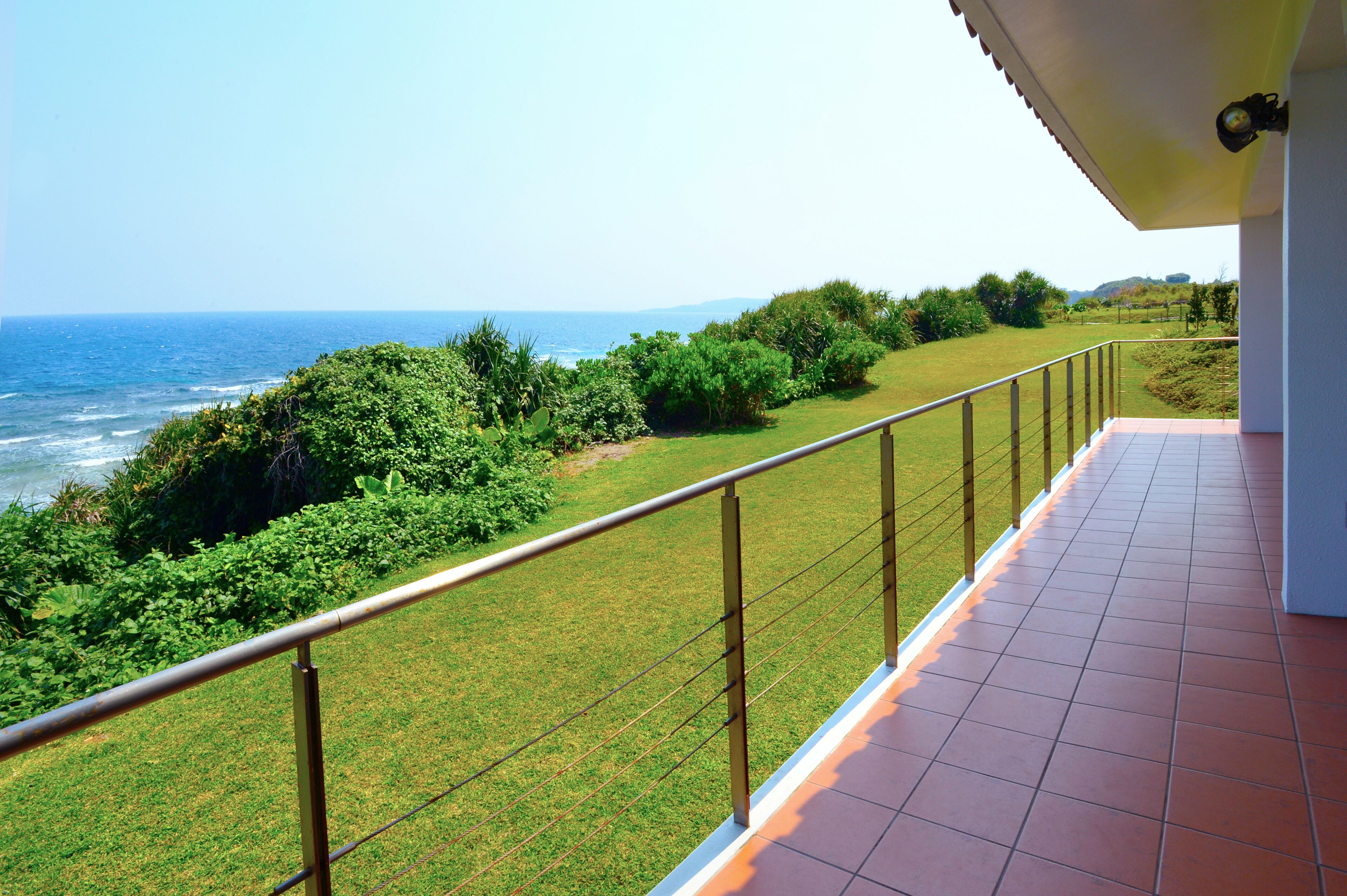 A balcony with a view of the ocean and greenery.
