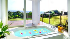 A bathroom with a large bathtub, a window with a view of the sea, and a potted plant. - wisteria ocean Nakijin (Nakijin)