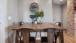 A dining area with a wooden table, four chairs, a wall clock, a sign, and a potted plant. - The West End Cottage (Buhl)