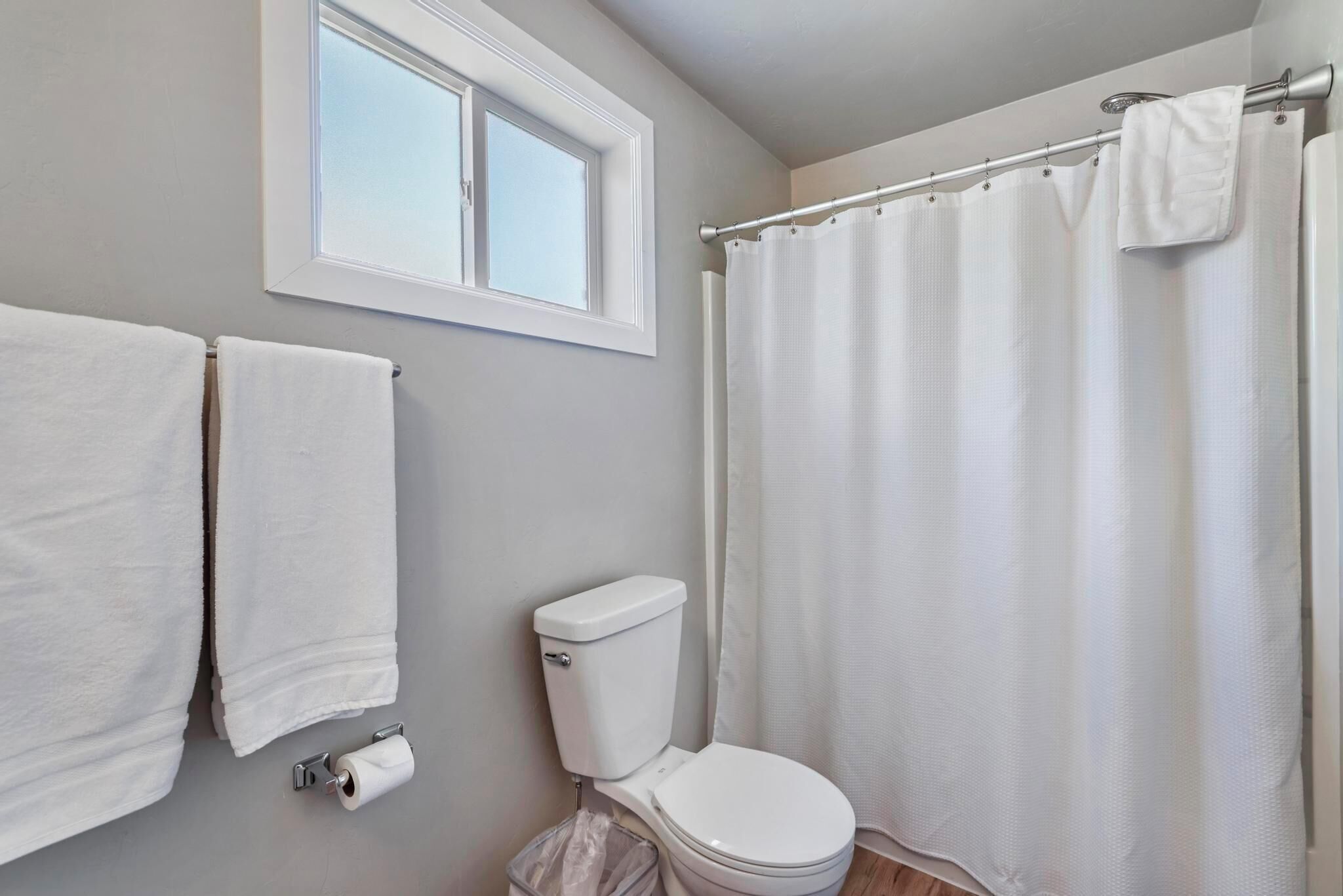 A bathroom with a toilet, a window, a shower curtain, and two towels hanging on the wall.