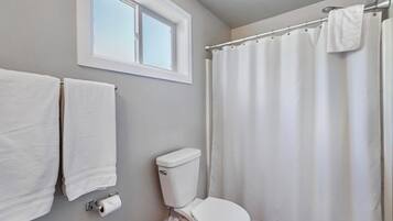 A bathroom with a toilet, a window, a shower curtain, and two towels hanging on the wall.