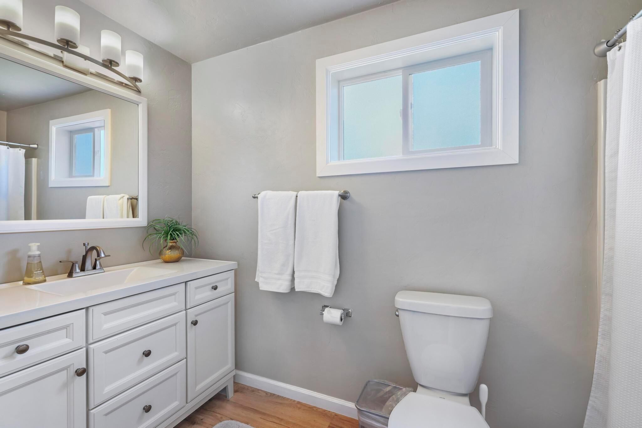 A bathroom with a toilet, sink, and mirror. There is a window above the toilet and a towel rack with towels.