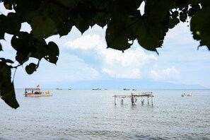 A calm body of water with several boats, including a docked boat with a flag and a smaller boat with a yellow container. - Local Beach Phu Quoc (Phu Quoc)