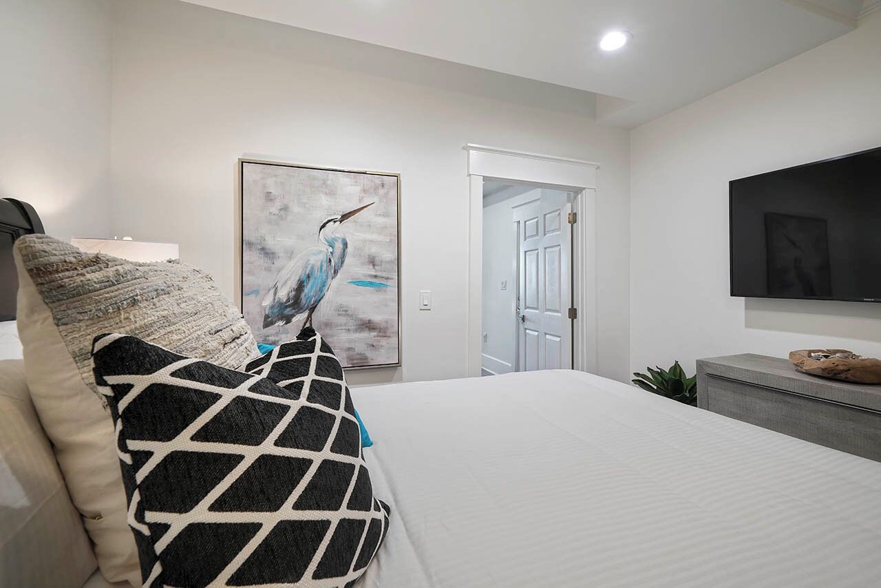 Une chambre moderne avec un grand lit, un tableau représentant un oiseau, une télévision et une porte donnant sur une autre pièce.
