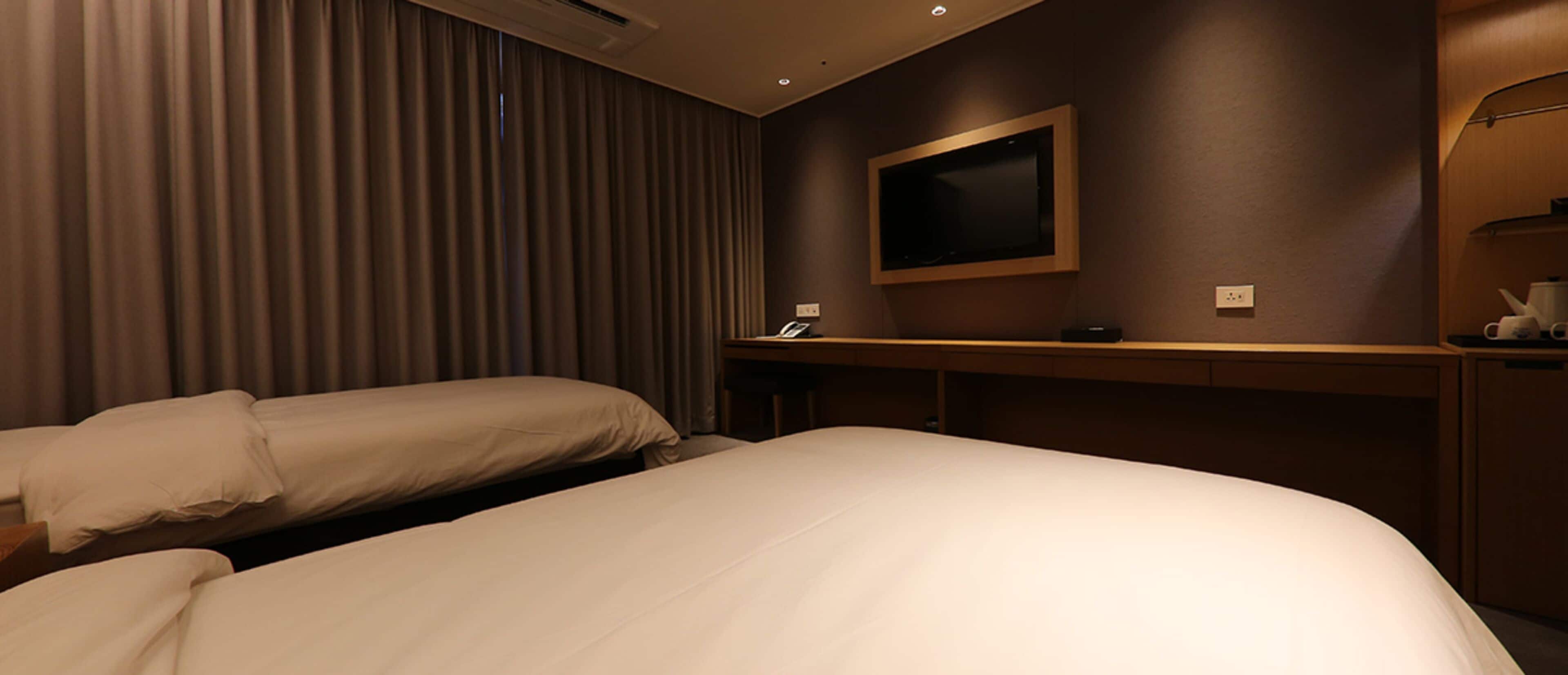 A hotel room with two beds, a flat-screen TV mounted on the wall, a desk with a telephone, and a minibar.