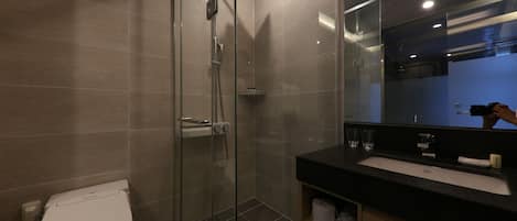 A modern bathroom with a glass-enclosed shower, a white toilet, and a black countertop with a sink and mirror.