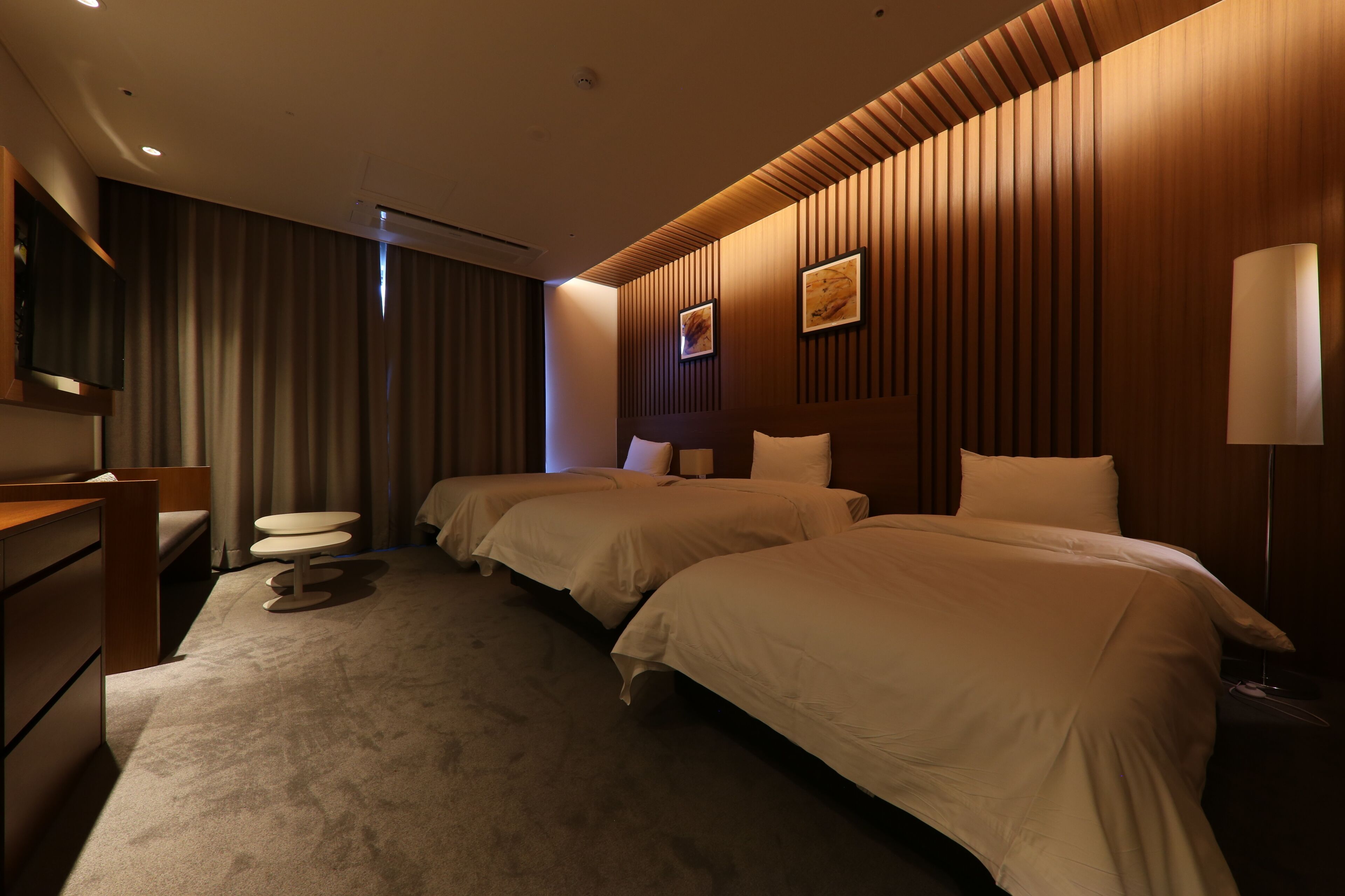 A hotel room with two beds, a desk, a chair, a small table, and a TV.