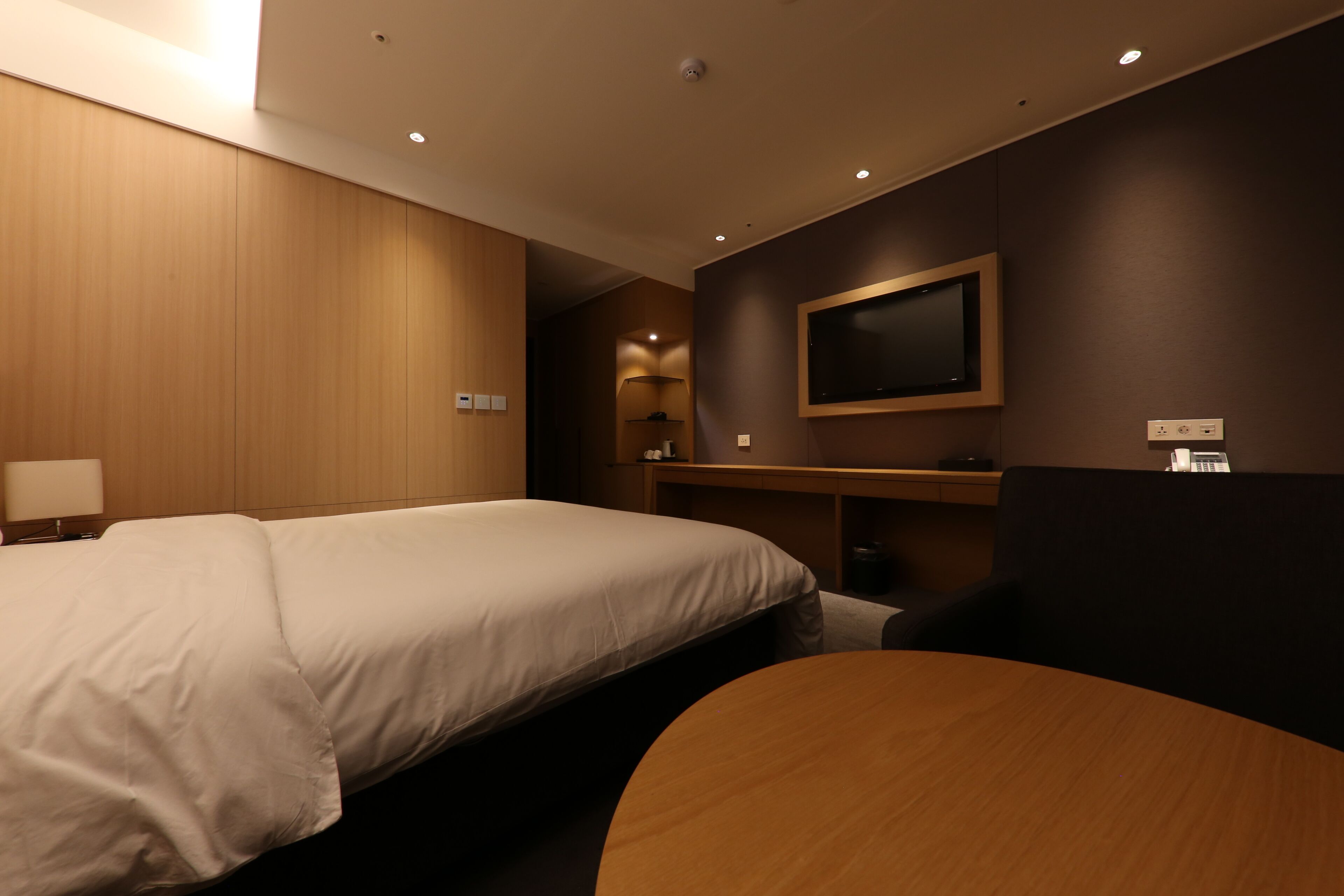 Ein Hotelzimmer mit einem großen Bett, einem an der Wand montierten Fernseher, einem Schreibtisch und einem Stuhl.
