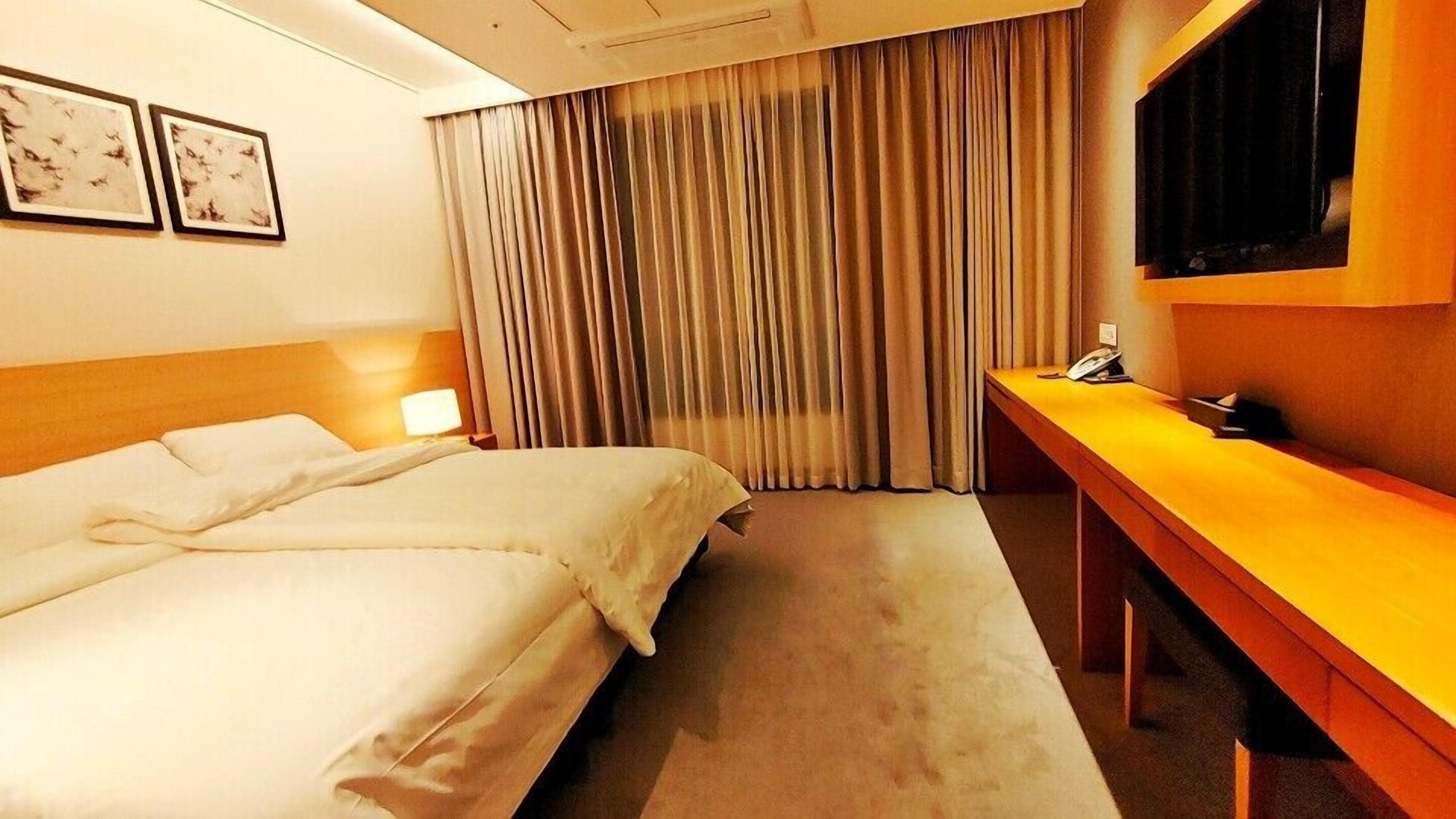 A hotel room with a bed, a desk, a TV, and curtains.
