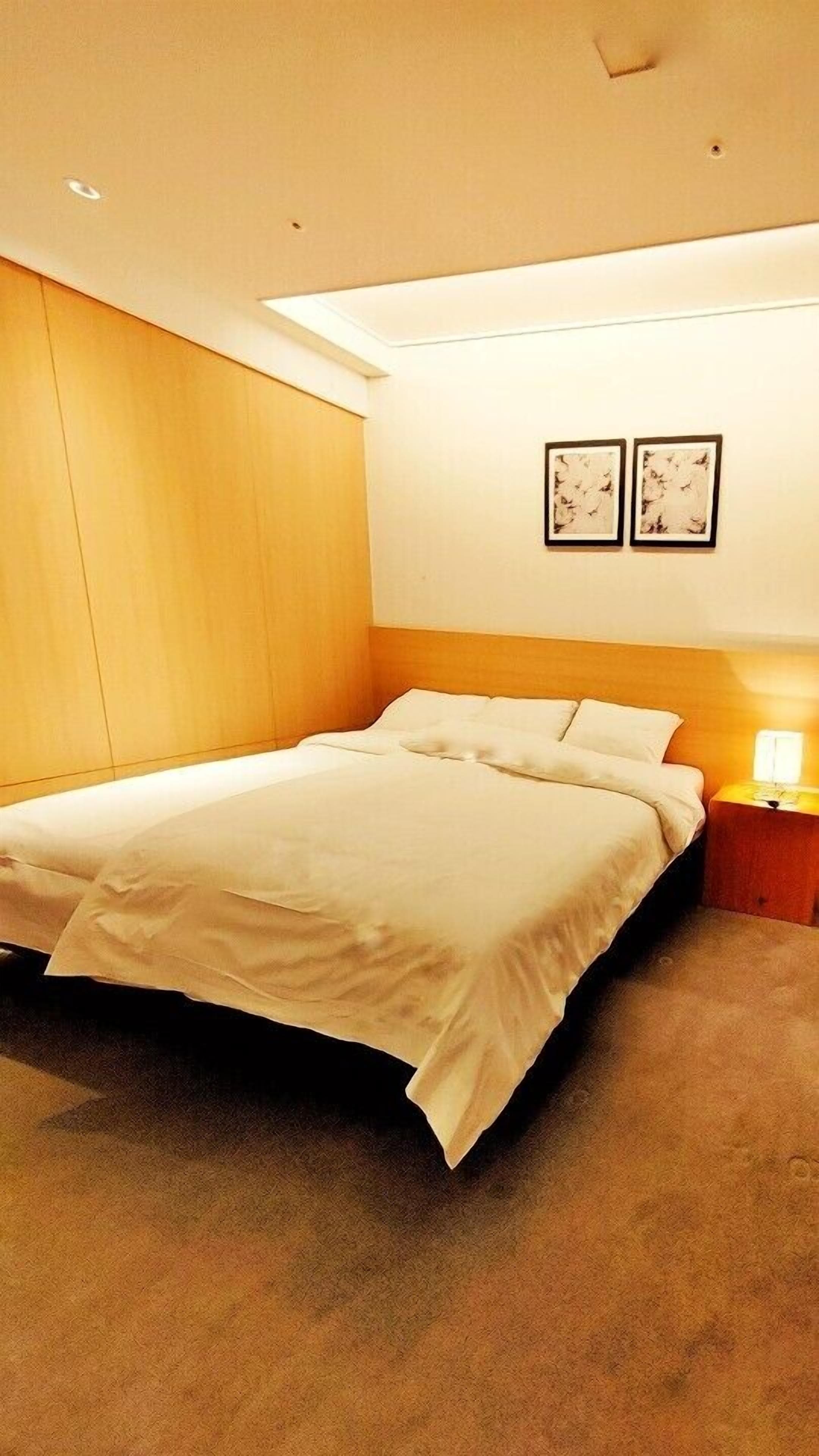 A hotel room with a bed, a nightstand with a lamp, and two framed pictures on the wall.