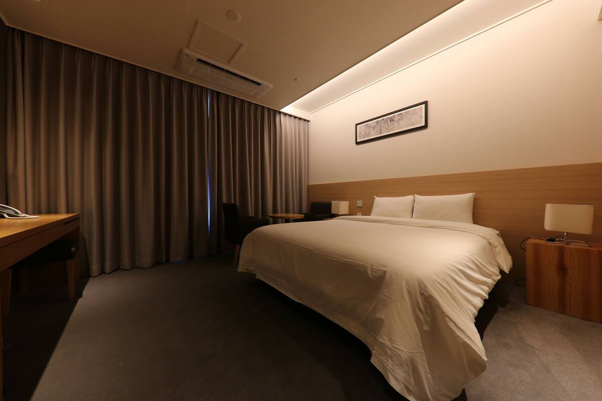 Habitación de hotel con una cama grande, un escritorio, una silla, una mesita y una lámpara.