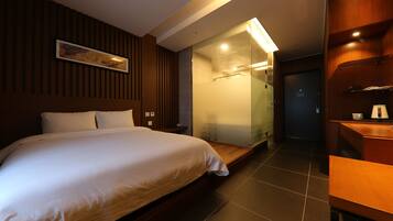 A modern hotel room with a large bed, a glass shower enclosure, and a wooden desk.