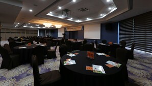 Un salón de conferencias con varias mesas redondas, sillas negras y una pantalla de proyector.