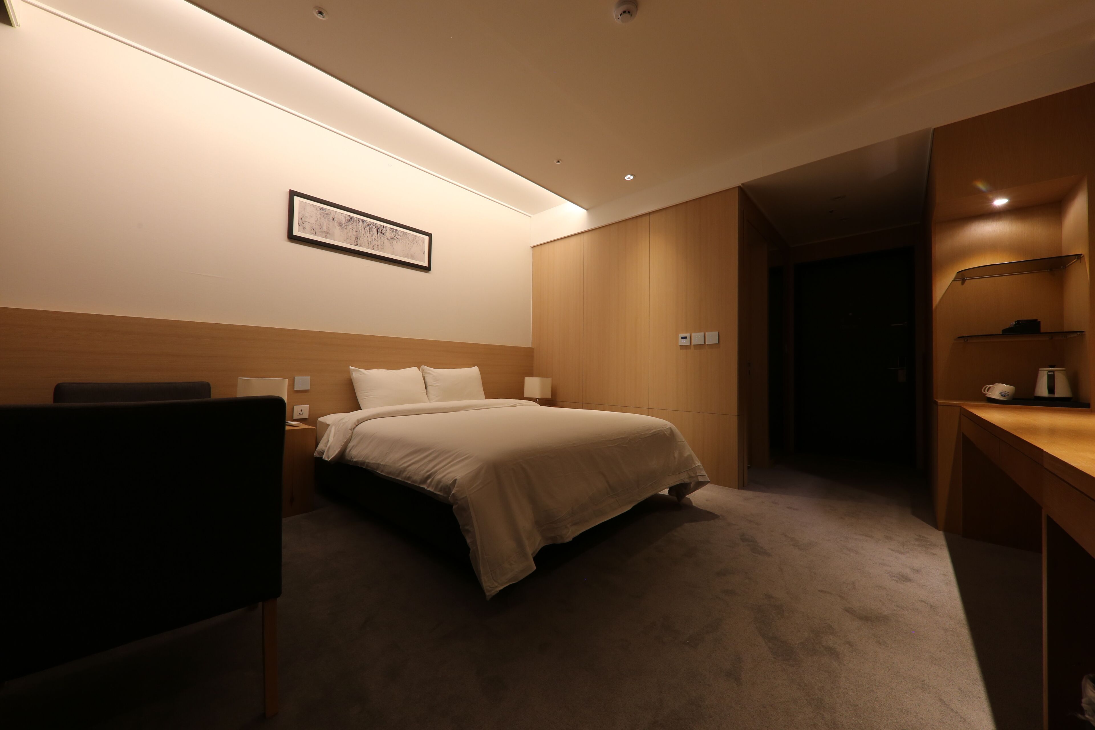 A hotel room with a bed, bedside table, lamp, and a framed picture on the wall.