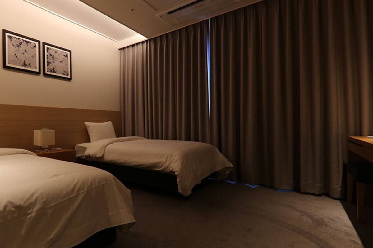 Habitación de hotel con dos camas, un escritorio, una mesita de noche y una ventana con cortinas.