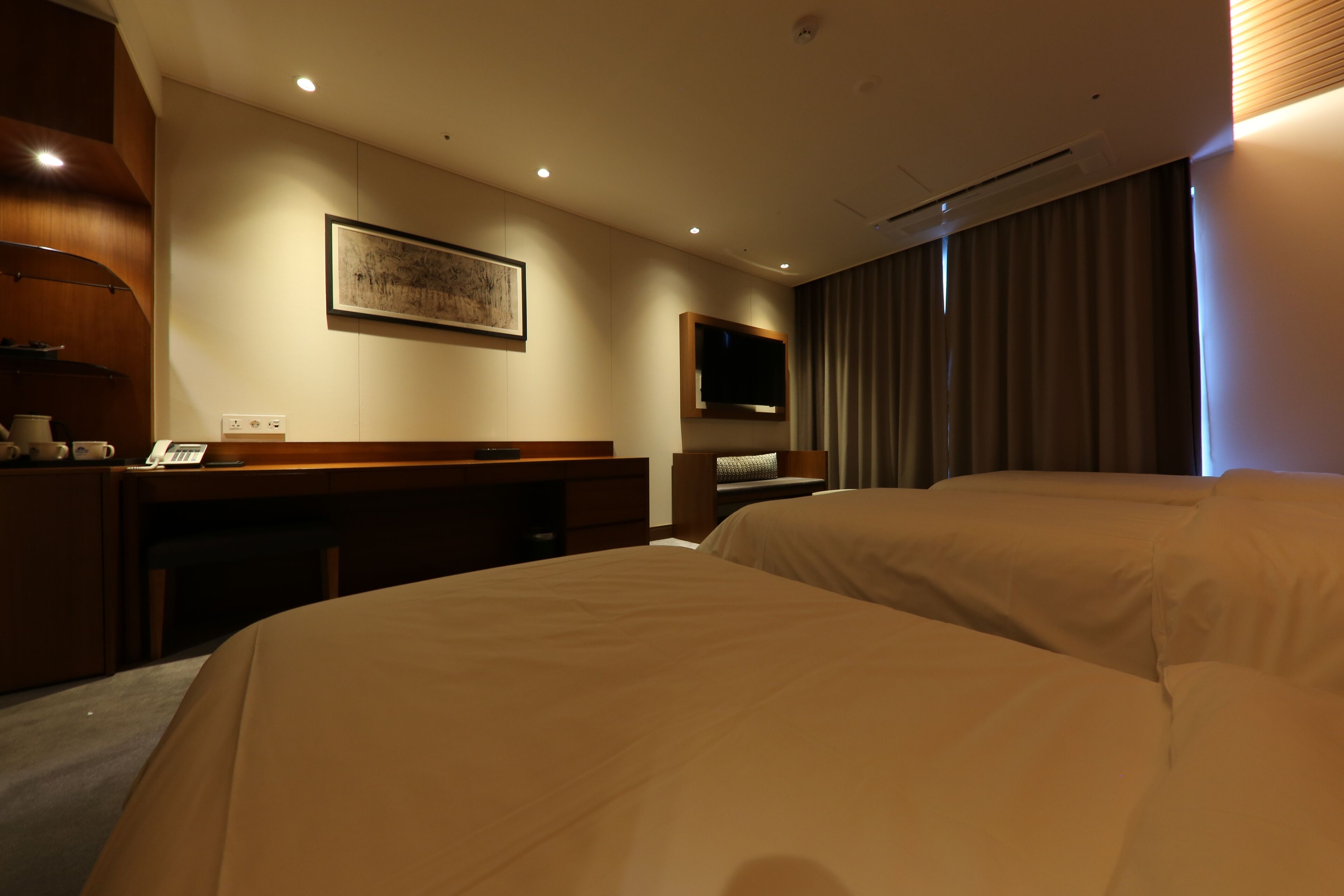 A hotel room with two beds, a desk, a flat-screen TV, and a painting on the wall.