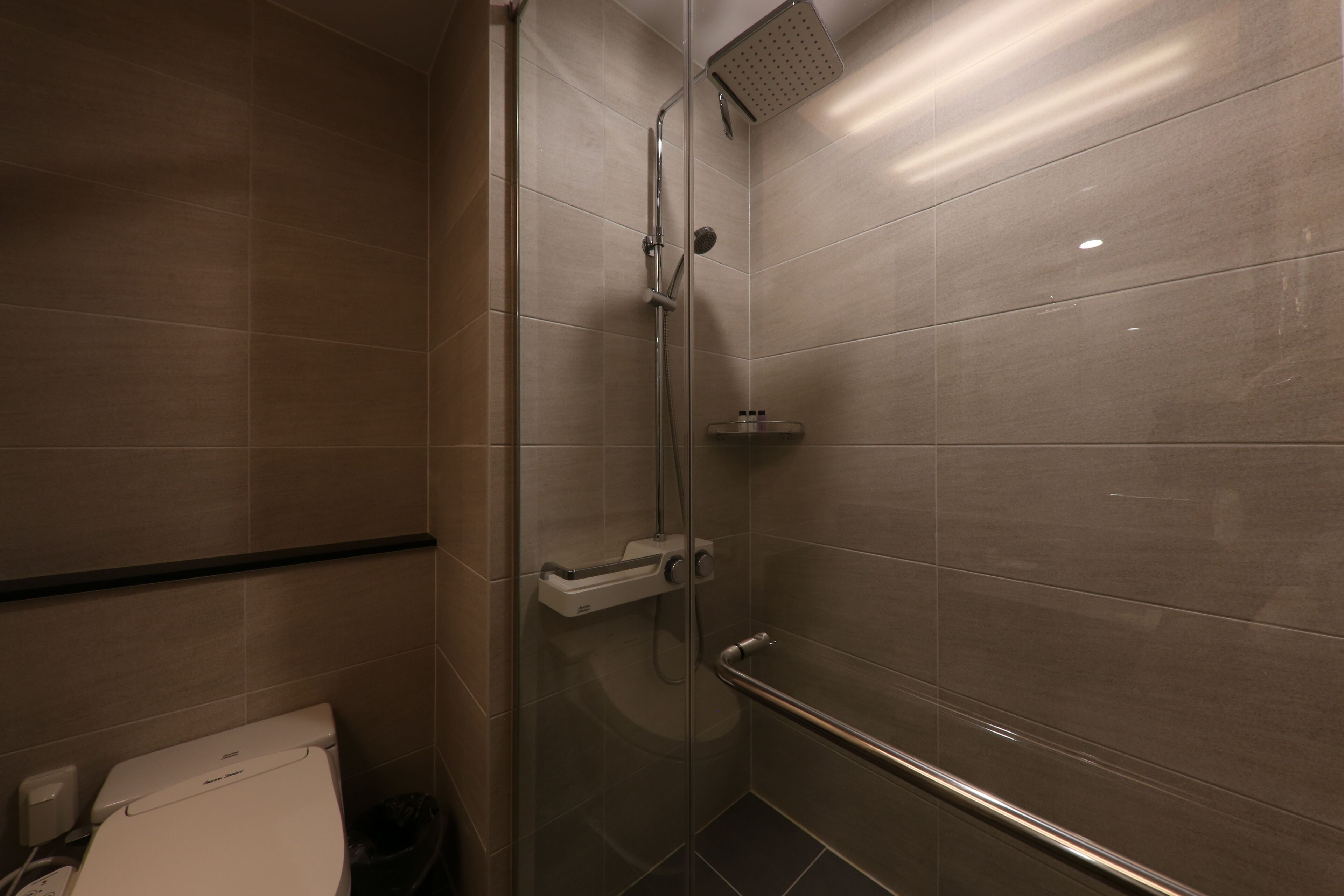 Un baño moderno con cabina de ducha de vidrio, inodoro y barra de apoyo.