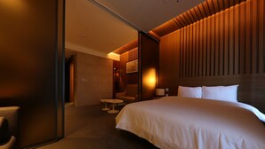 Una habitación de hotel con una cama grande, una silla, una mesita y un televisor montado en la pared.