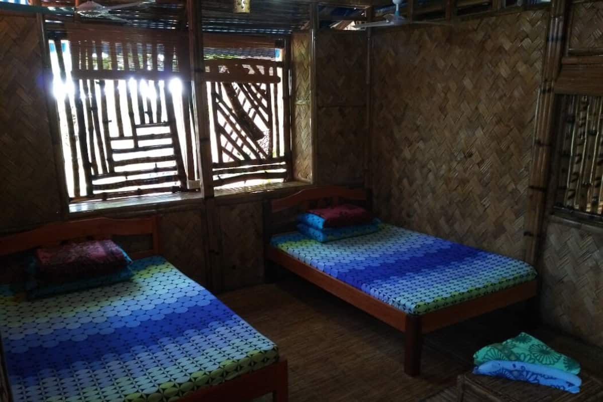 Ein Zimmer mit zwei Holzbetten, einer gewebten Wand und einem Fenster mit Holzgitter.