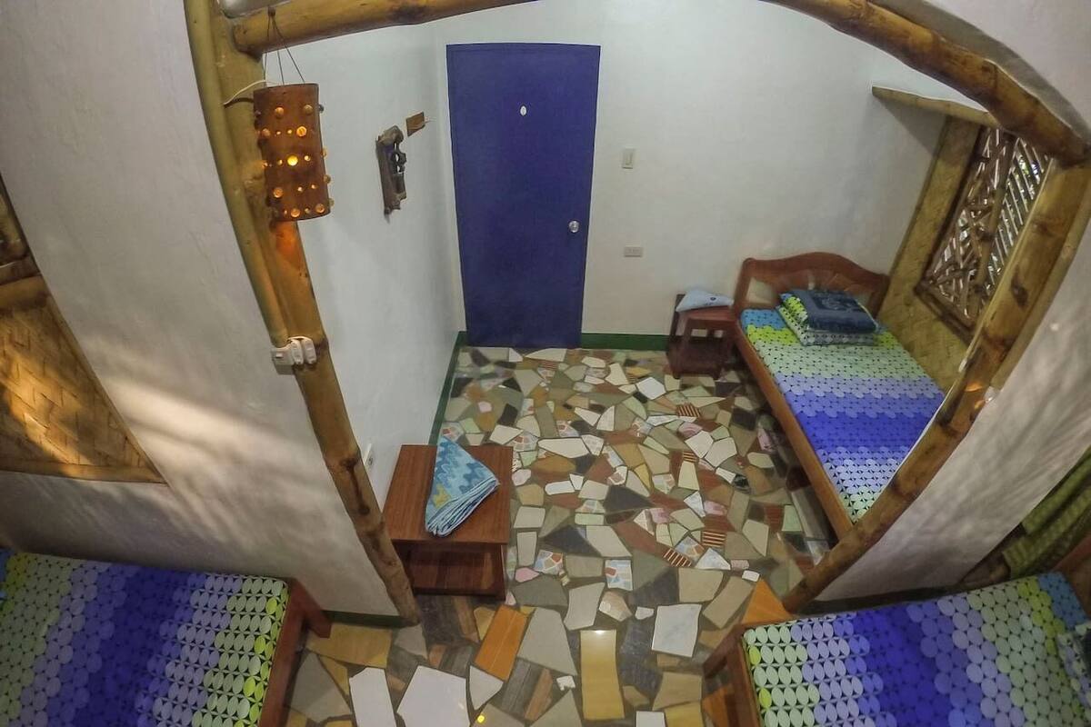 Ein kleiner Raum mit einer blauen Tür, einer Holzbank, einem kleinen Tisch mit einer zusammengefalteten Matte und einem fußbodenartigen Mosaikboden.